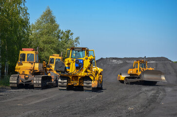 Crawler dozers on a coal heap. Mining machines moving clay, smoothing the surface of gravel for a new road. Earthworks, excavations, digging in the soil