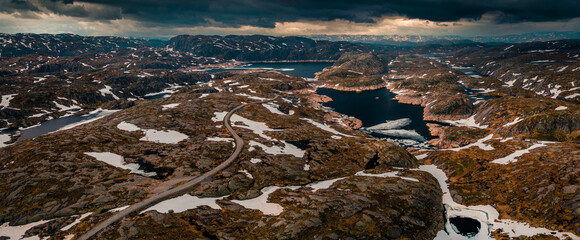 Landscape with lonesome road from above around Lysefjord in Rogaland with lakes and snow in Norway, dark cloudy sky