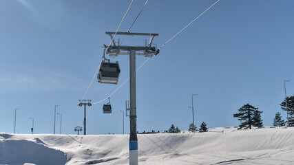 Gondola lift - cable car in the mountain tourist center. Snow covered ground, blue sky, sunny day