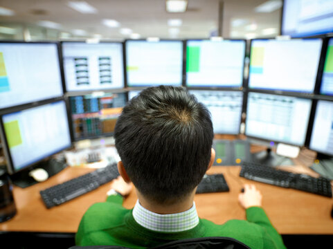 A Man Looking At Multiple Trade Screens At His Desk.