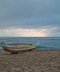 Fototapeta na wymiar Tan and White Outrigger Canoe on the Edge of the Sea in a Rain Shower.