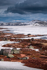 Hut at the waterfront of a frozen lake in the landscape of Hardangervidda National Park in Norway, snow and ice on the ground