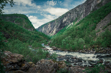 Naklejka na ściany i meble River currents in the valley of Voringsfossen waterfall at Hardangervidda National Park in Norway, steep mountains aside, green vegeation