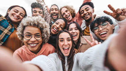 Multicultural community of young people smiling together at camera - Happy diverse friends taking selfie picture with smart mobile phone device - Friendship and human relationship concept