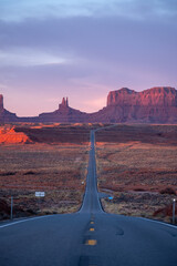 Monument Valley long road into the desert, towering stone structures in the distance