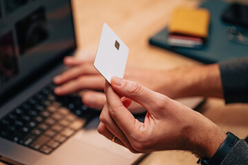 Close-up shot of male hands holding white blank credit card while typing with the other on the keyboard. Online shopping or payment.
