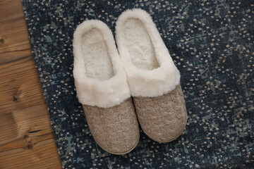Pair of beautiful soft slippers and rug on wooden floor, top view