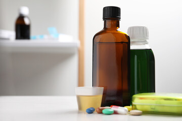 Bottles of syrup, measuring cup and pills on table, space for text. Cold medicine
