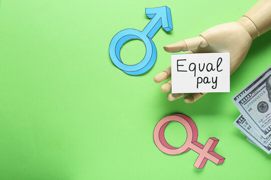 Equal pay. Wooden mannequin hand, dollar banknotes, paper note, gender symbols on green background, flat lay with space for text