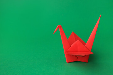Red paper origami crane on green background, space for text