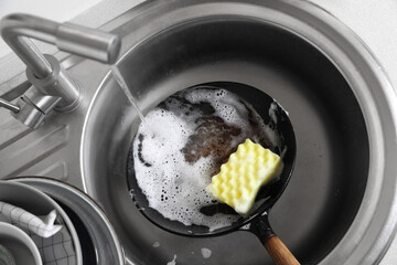 Dirty frying pan with sponge in kitchen sink, above view