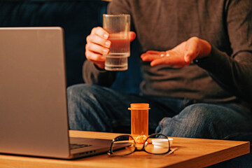 Unrecognizable man taking medicine while working at the laptop.