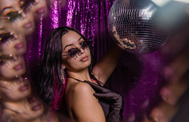 fashion beauty model with sunglasses wearing all black holding disco ball in front of sequin...