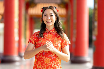 Asian woman in red cheongsam qipao dress is paying respect and gratitude inside Chinese Buddhist temple during lunar new year for  for best wish blessing and good luck concept