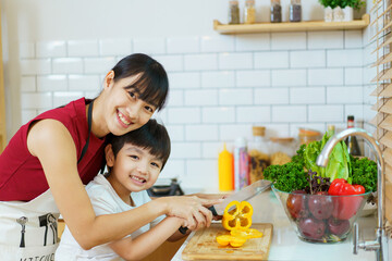 Happy cheerful mother and her little boy preparing a foods and vegetables in domestic kitchen together. 