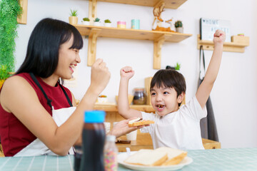 Happy little young boy and his mother making an easy breakfast together in a kitchen with a breads and chocolate jam. 