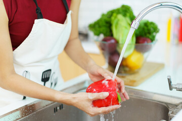 Happy healthy Asian woman washing a vegetables in domestic kitchen faucet before cooking. 