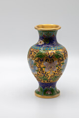 Macro view of a small antique cloisonne vase with multicolored enamel on a gold base, showing wear from age, on white background