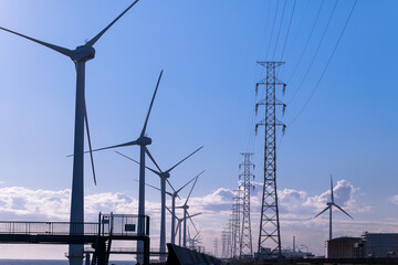 中央の送電線を挟んで風力発電と石油タンクの脱炭素対比の風景