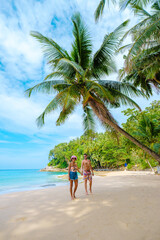 A couple of men and women walking on a white tropical beach with palm trees in Phuket Thailand....
