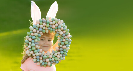 Child boy with easter eggs and bunny ears outdoor. Cute kid having happy easter in park. Funny kids face closeup. Horizontal photo banner for website header design.