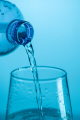Water pouring from a plastic bottle into a glass beaker on a blue background