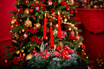 Three burning red candles against the background of a Christmas tree bokeh, lights and decorations. Concept of christmas and new year.