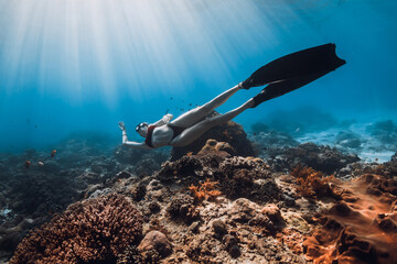 Woman freediver with diving fins glides on coral reef. Freediving in blue ocean with sun rays