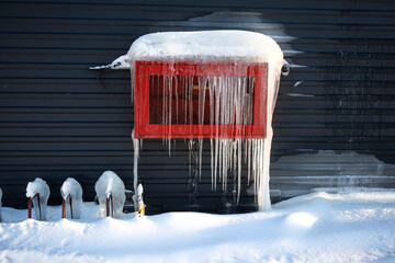 A fire hose cabinet mounted outside on the wall of a building is all covered and blocked by snow,...