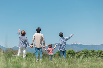 空と高原・草原・公園で手を繋ぐアジア人の三世代家族・親子・ファミリーの後ろ姿
