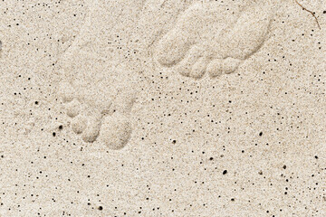 Woman footprint close up on sand on seashore. Imprint female bare feet on white beige sand. Summer rest or vacation on beach concept. Top view natural sandy texture with footsteps