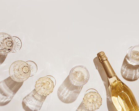 Top view white sparkling wine in different glasses of wine, stemmed glass with sun shadow and glare on light beige background. White wine tasting concept flat lay, copy space. Summer drinks