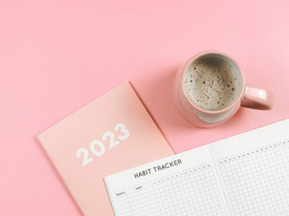  flat lay of habit tracker book on pink diary or planner 2023 and pink cup of coffee on pink...