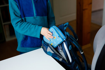 School kid boy getting ready in the morning for school. Healthy child filling satchel with books, pens, folders and school stuff. Preaparation, routine concept.