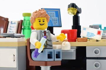 Naklejka premium Lego minifigure of young boss or office manager with pen on the table with pc laptop and chaos closed up 