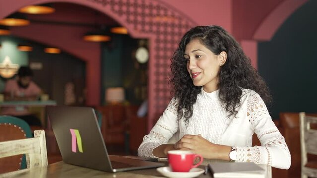Beautiful Indian girl watching funny videos,movie or social media content on a laptop while sitting in the restaurant.Pretty  Asian woman looking at laptop screen and watching something funny indoor.
