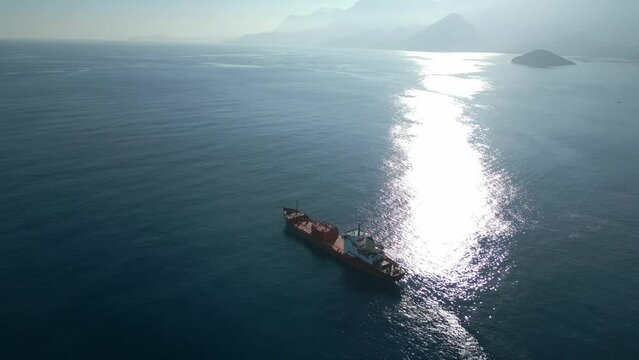 The camera flies around a chemical tanker drifting at sunset near the coastline with mountains. High quality 4k footage