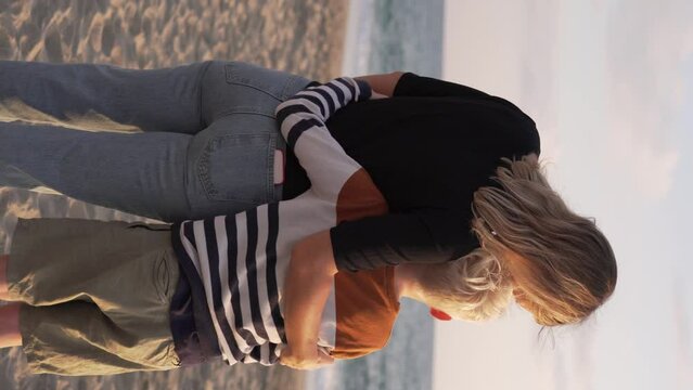 Vertical video, beautiful mother hugs a white boy on the sea, Mother and son dancing and having fun on the beach.