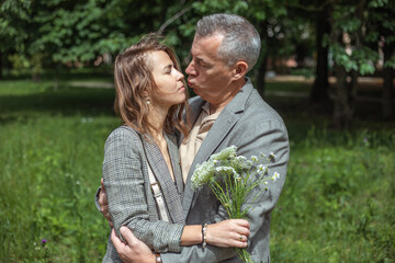 Romantic couple of upset, depressed woman holding bouquet of field flowers, mature man try to kiss female in green park