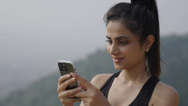 close-up Indian female chatting with friend on Smart Phone at the mountain. young Woman holding smart phone using mobile apps watching funny video.Smiling Asian girl having fun chatting. 