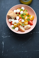 Roseate bowl with mini mozzarella and tomato salad, top view on a black marble background, vertical shot, copyspace