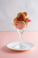 Heart-shaped cookies with jam filling in a martini glass on a pink plain background. Valentine's day concept.