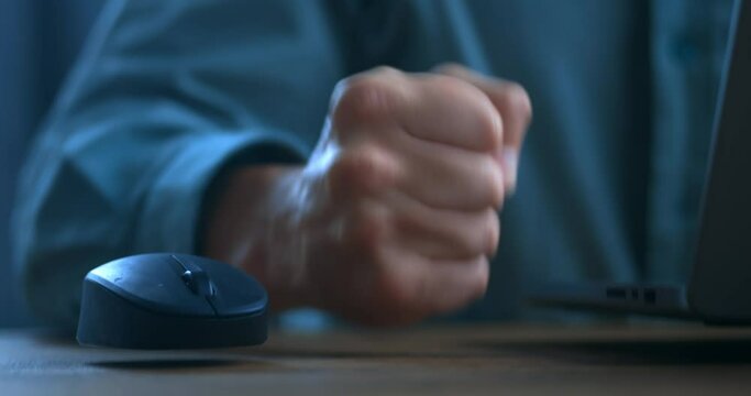 Angry business man is dissatisfied with the work at the computer mouse and hits the table with his fist. The concept of showing anger while working at a laptop, close-up. Problems with online business