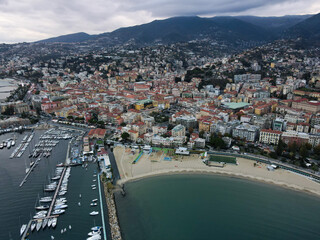 Aerial view of Sanremo, Italian city on the seashore in Liguria, north Italy. Drone flying along the port over beaches and boardwalk with palm trees and Birds Eye of yacht parking in San Remo, Italy.