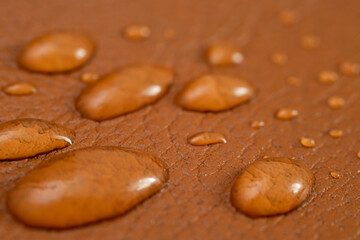 Round water drops on brown leather texture, side view