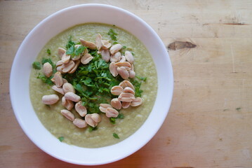 Bowl of white soup with parsley and peanuts on a wooden background