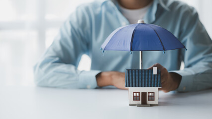 Individuals holding small umbrellas and model homes, housing insurance against impending loss and...