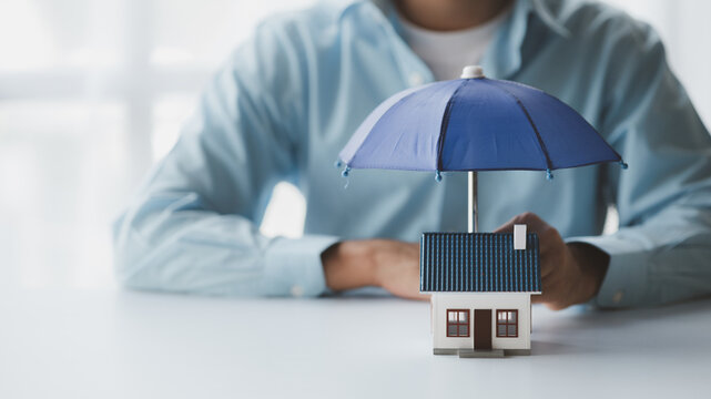 Individuals holding small umbrellas and model homes, housing insurance against impending loss and fire, building fire insurance, home and real estate insurance concepts.