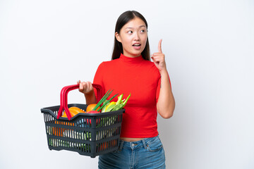Obraz na płótnie Canvas Young Asian woman holding a shopping basket full of food isolated on white background thinking an idea pointing the finger up