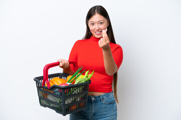 Fototapeta na wymiar Young Asian woman holding a shopping basket full of food isolated on white background making money gesture